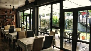 Un espace de restauration intérieur avec des tables et des chaises, de grandes fenêtres et un mur en briques agrémenté d’étagères.