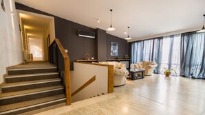 Un salon moderne avec un escalier, un canapé, une table basse et une grande fenêtre avec des rideaux.
