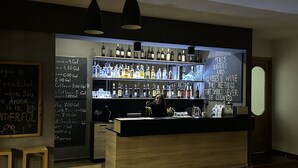 Un espace bar avec un comptoir en bois, des étagères remplies de différentes bouteilles d’alcool et un menu écrit à la craie.