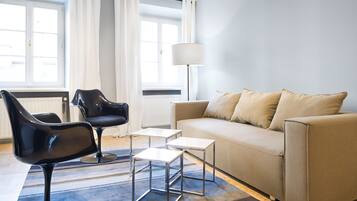 Ein modernes Wohnzimmer mit einem beigen Sofa, schwarzen Ledersesseln, einem weißen Beistelltisch und einer Stehlampe.