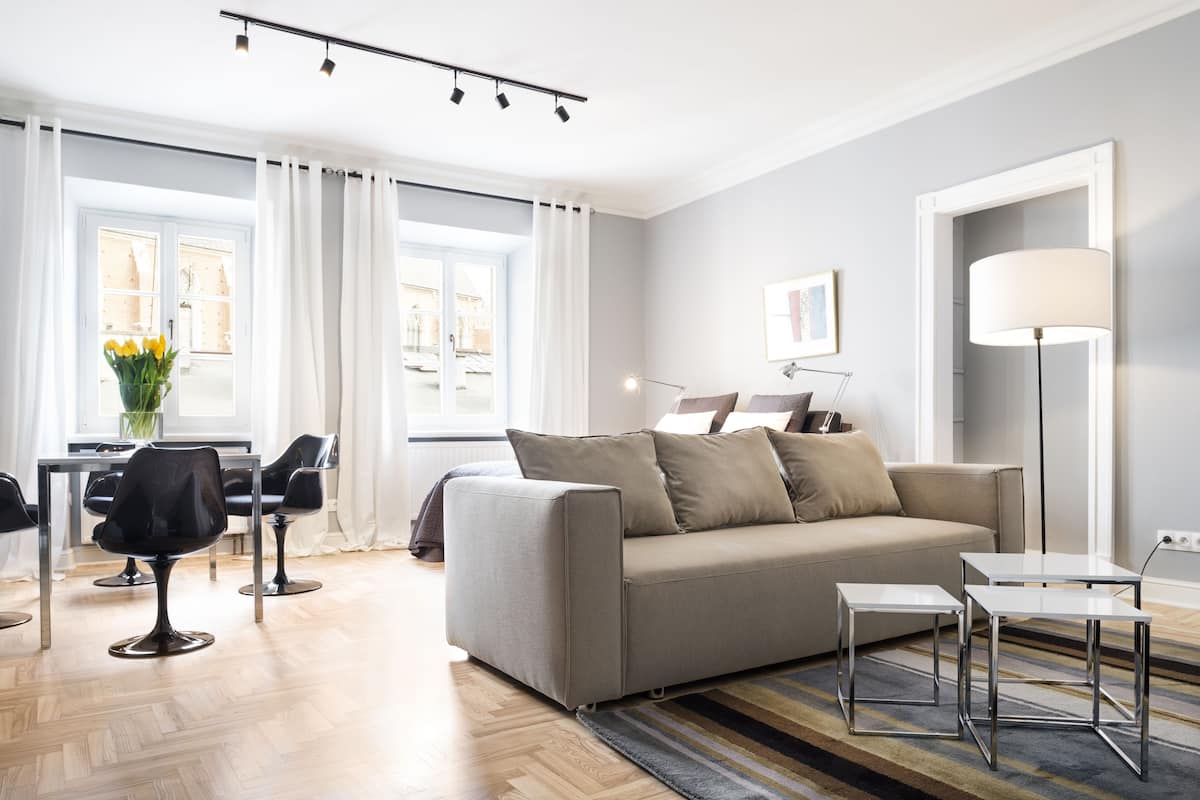 A modern living room with a sofa, two side tables, a floor lamp, and a dining area with chairs and a table.