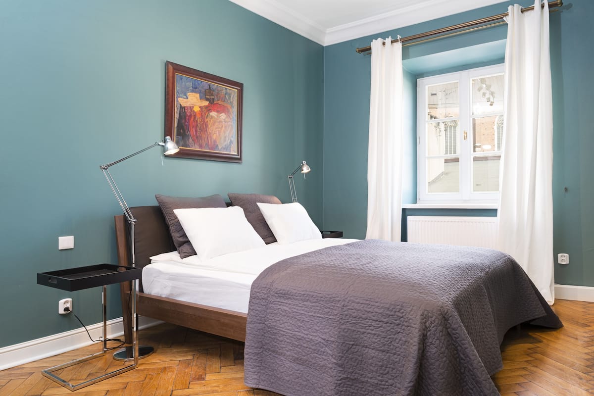 A bedroom with a bed, bedside tables, a painting on the wall, and a window with curtains.