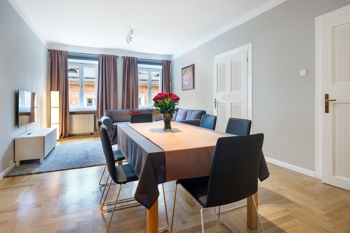 A modern dining area with a wooden table, black chairs, and a vase of red flowers.