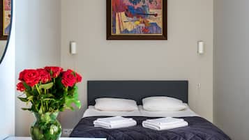 Una cama bien hecha con un edredón oscuro, un jarrón de rosas rojas y un cuadro en la pared.