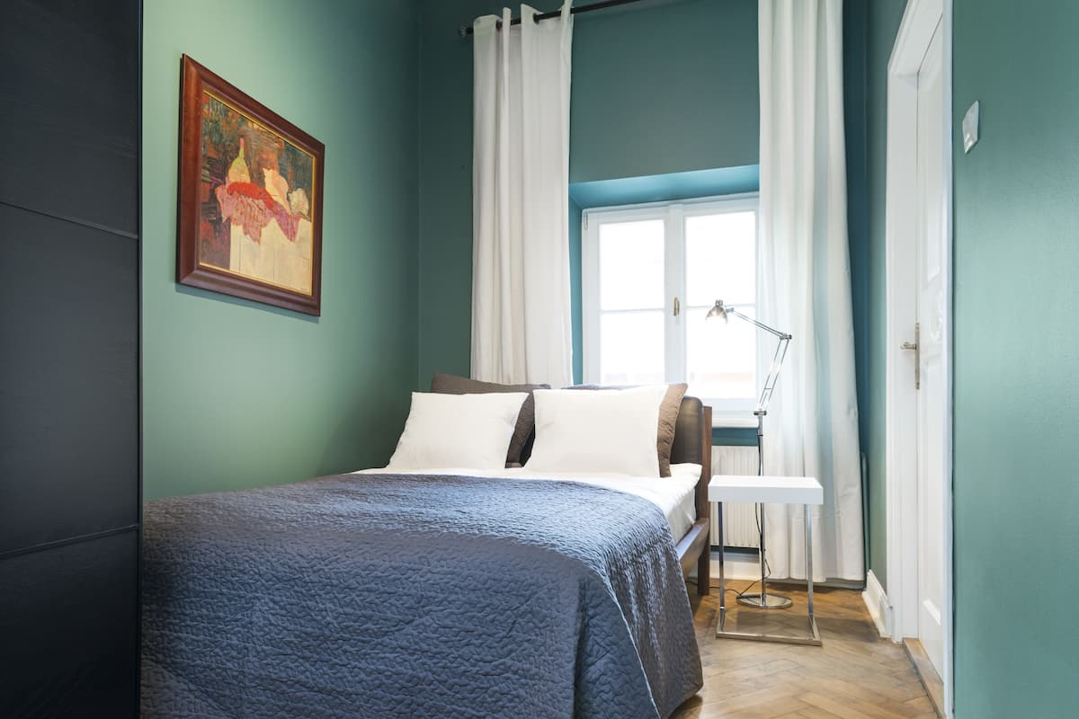 A bedroom with a bed, a desk, a lamp, and a window with curtains.