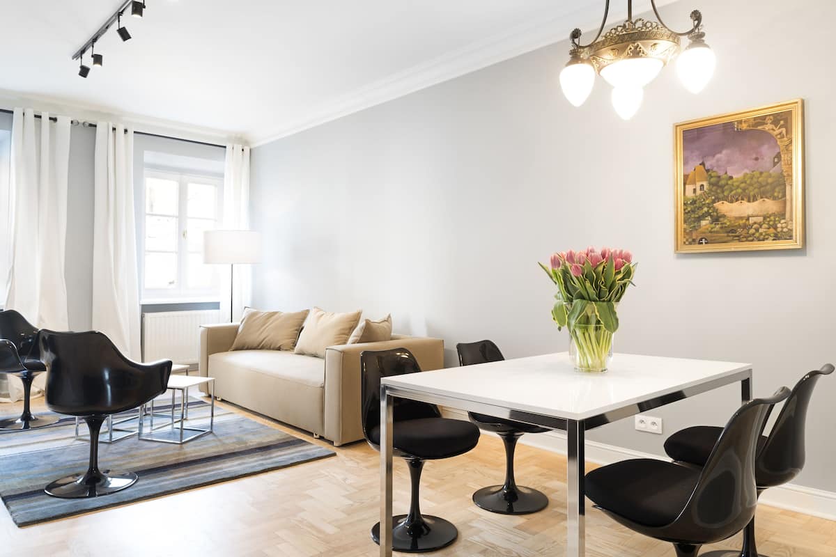 A modern living room with a dining table, black chairs, a beige sofa, and a vase of flowers.