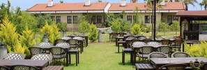 An outdoor seating area with multiple tables and chairs, surrounded by greenery and a building with a tiled roof. - Nerissa Hotel - Special Class (Kemer)