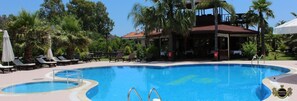 A swimming pool with lounge chairs and umbrellas, surrounded by palm trees and a building with a red roof. - Nerissa Hotel - Special Class (Kemer)