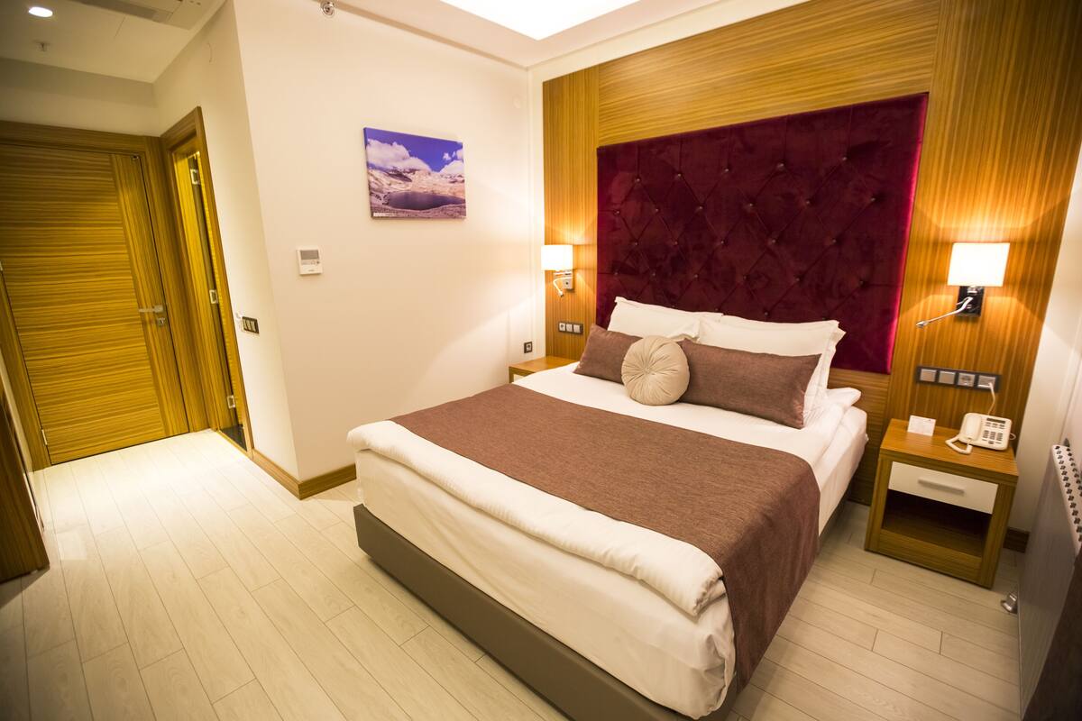 Habitación de hotel con una cama grande, cabecera de madera, dos mesitas de noche con lámparas y un cuadro en la pared.
