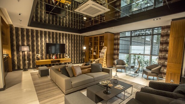 A modern living room with a sofa, coffee table, and chairs, a TV, and a bookshelf. - Honour Hotel (Nigde)