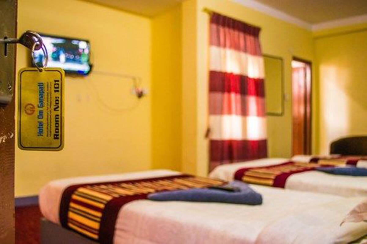 A hotel room with two beds, a television mounted on the wall, and a red and white striped curtain.