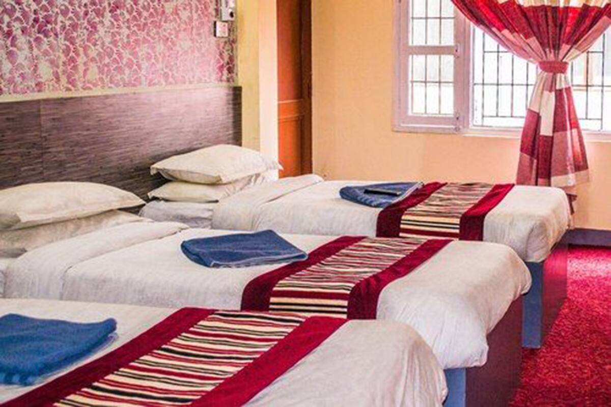 A hotel room with three beds, each with white bedding and striped blankets.