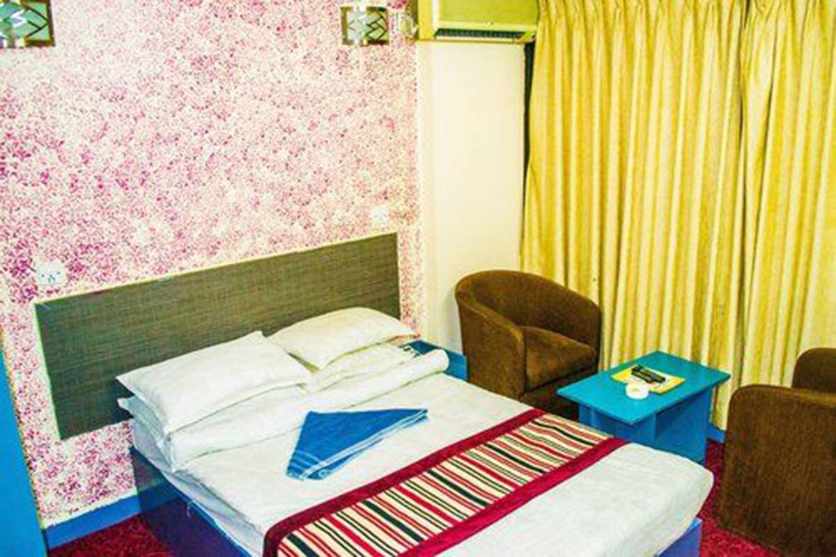 A hotel room with a bed, a chair, a small table, and a curtain.