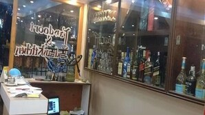 A room with a desk, a laptop, and a window displaying various bottles. - Thamel Trekkers Hotel (Kathmandu)