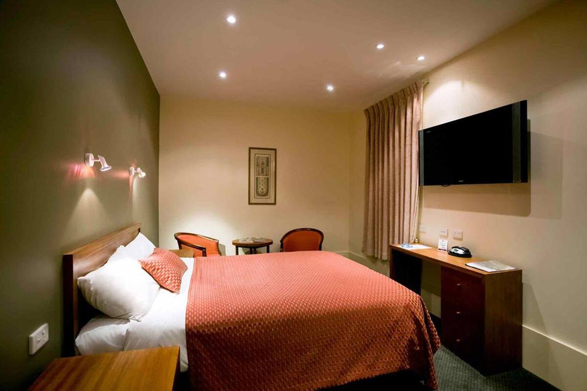 A hotel room with a bed, a desk, a chair, a television, and a small table.