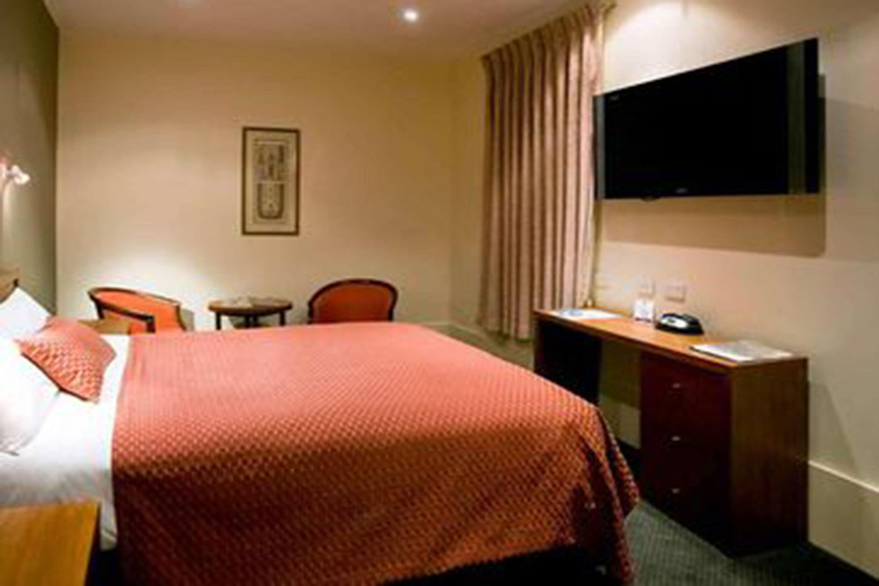 Habitación de hotel con cama, escritorio, silla, televisión y un cuadro en la pared.