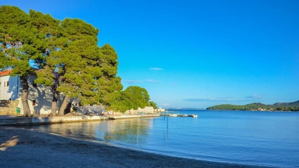 A coastal scene with a sandy beach, a row of trees, and a building with a red roof. - Villa Stari dvor (Preko)
