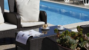 A poolside area with wicker furniture, a table with a menu, and a potted plant. - Villa Stari dvor (Preko)
