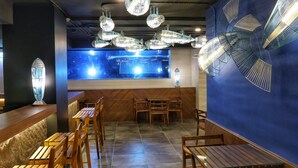 L’intérieur d’un restaurant avec un mur bleu, des meubles en bois et des luminaires suspendus.