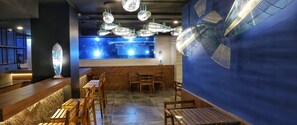 A restaurant interior with a blue wall, wooden furniture, and hanging light fixtures. - Stay With Nimman Chiang Mai (Chiang Mai)