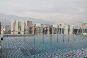 A rooftop swimming pool with a tiled floor and a view of modern buildings and mountains in the background. - Stay With Nimman Chiang Mai (Chiang Mai)