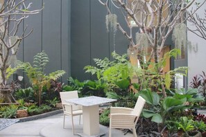 A patio with a table and chairs, surrounded by various plants and a tree with hanging moss. - Stay With Nimman Chiang Mai (Chiang Mai)