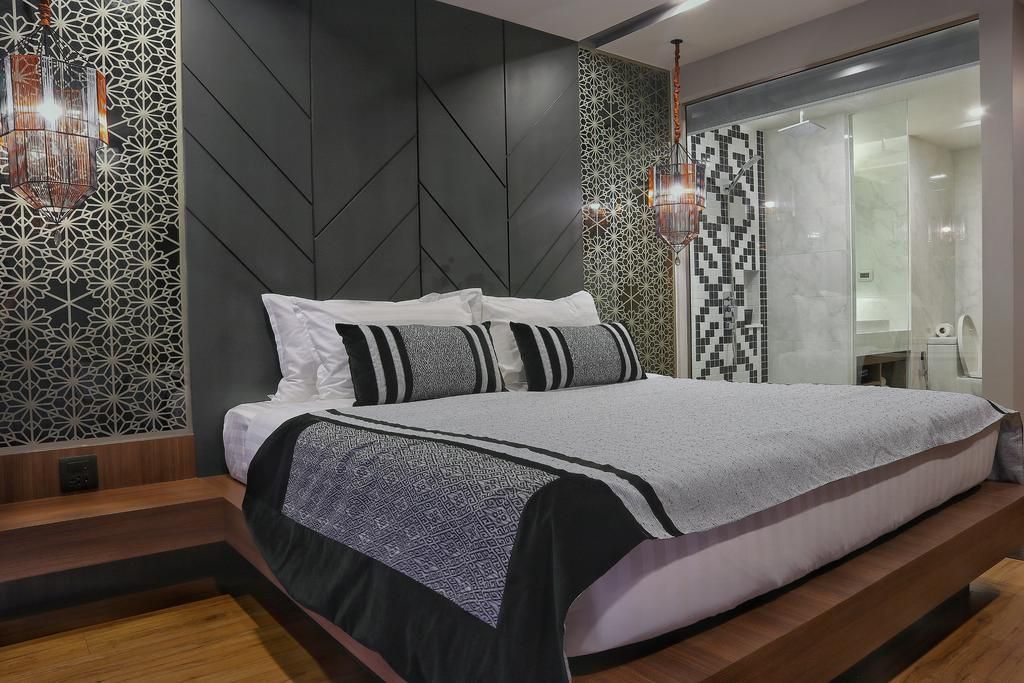 A modern bedroom with a bed, patterned walls, and a glass shower area.