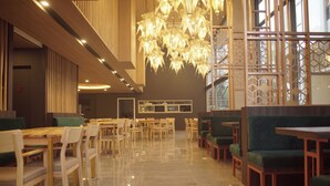Un ampli restaurant amb taules i cadires de fusta, un gran candelabrum i una vista per una finestra amb un disseny decoratiu.