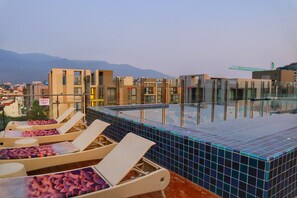 A rooftop infinity pool with lounge chairs, a tiled edge, and a view of buildings and mountains in the background. - Stay With Nimman Chiang Mai (Chiang Mai)