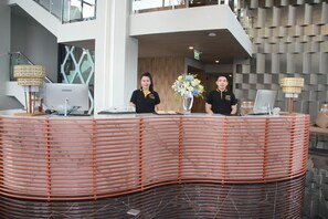 A reception desk with two staff members, a modern interior with a staircase, and a decorative vase with flowers. - Stay With Nimman Chiang Mai (Chiang Mai)