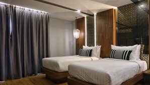 Habitació d'hotel amb dos llits, terra de fusta, un finestral gran amb cortines i un panell decoratiu a la paret.