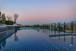 A rooftop pool with a glass barrier, a tiled floor, and a view of buildings and trees. - Stay With Nimman Chiang Mai (Chiang Mai)