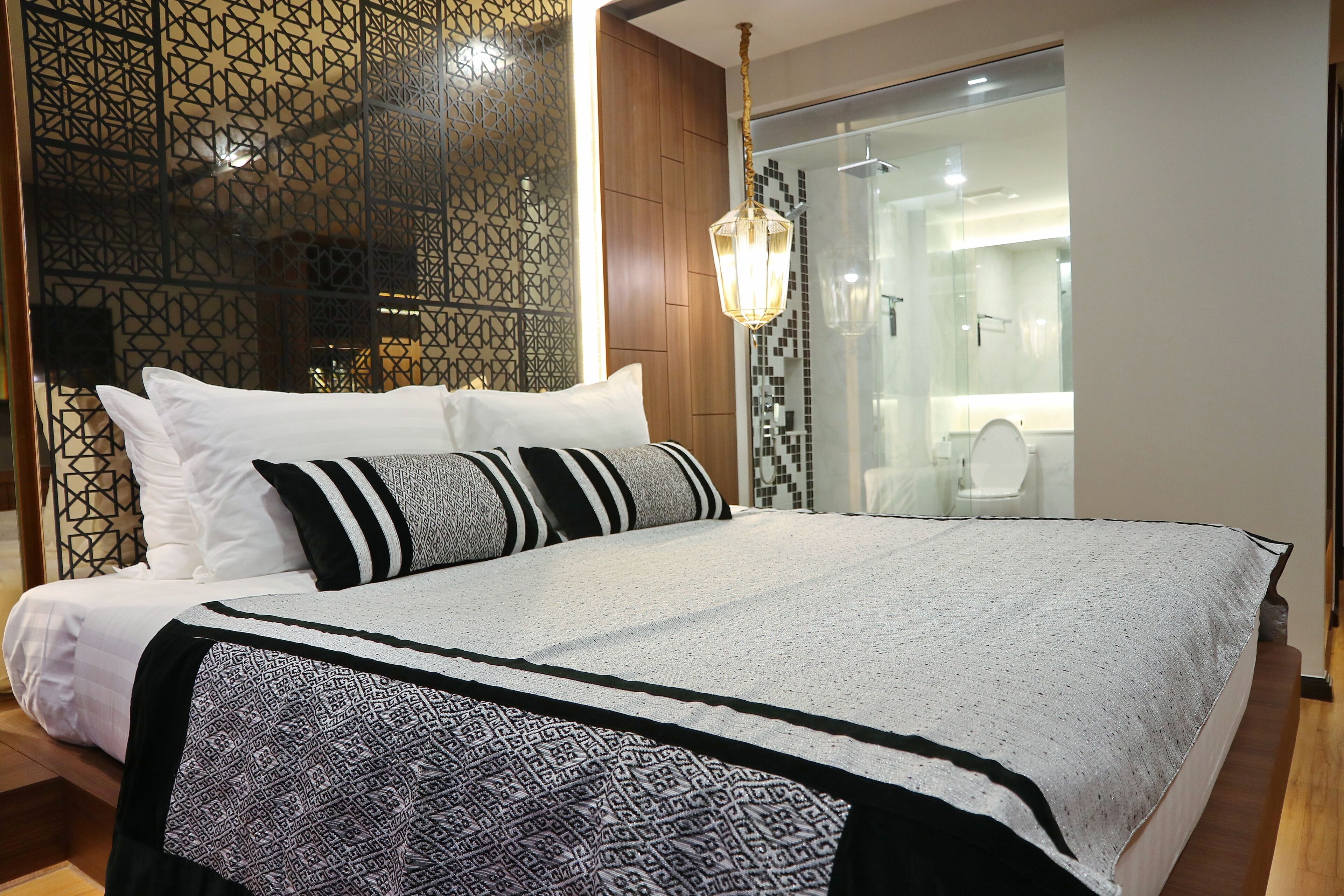 A neatly made bed with patterned bedding, a hanging light fixture, and a glass shower door.
