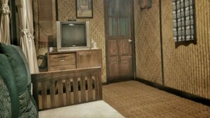 A room with a wooden cabinet, a television, a door, and a patterned wall. - Mon Saeng Jun Homestay (Phrao)