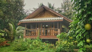 A wooden house with a balcony, surrounded by lush greenery and fruit trees. - Mon Saeng Jun Homestay (Phrao)
