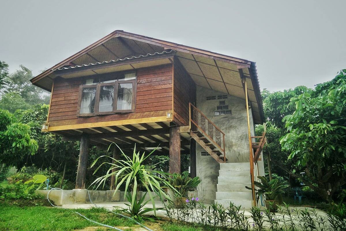 A wooden house with a balcony and a staircase leading to a concrete platform.