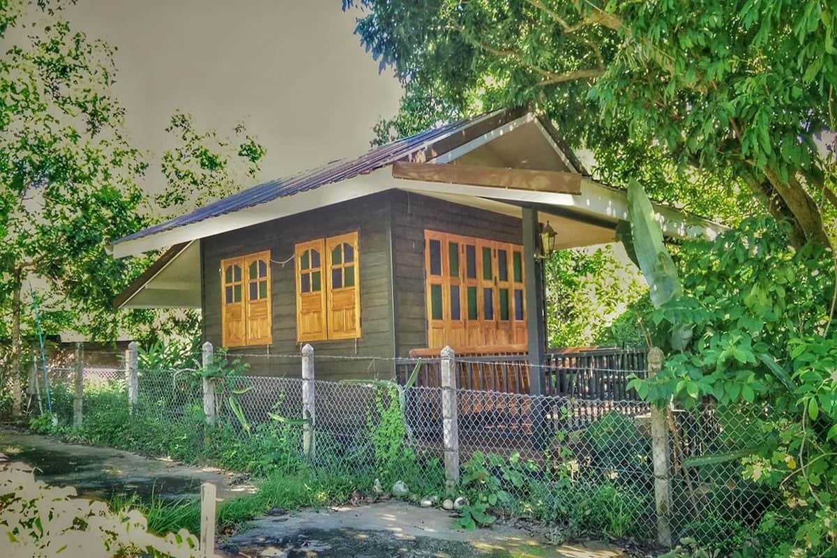 A wooden house with a porch, surrounded by a chain-link fence and lush greenery.