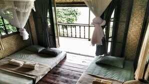 A room with two beds, a wooden floor, and a balcony with a view of greenery. - Mon Saeng Jun Homestay (Phrao)