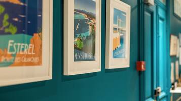 A hallway with framed artwork on teal walls, a door with a red handle, and a small table with items on it.