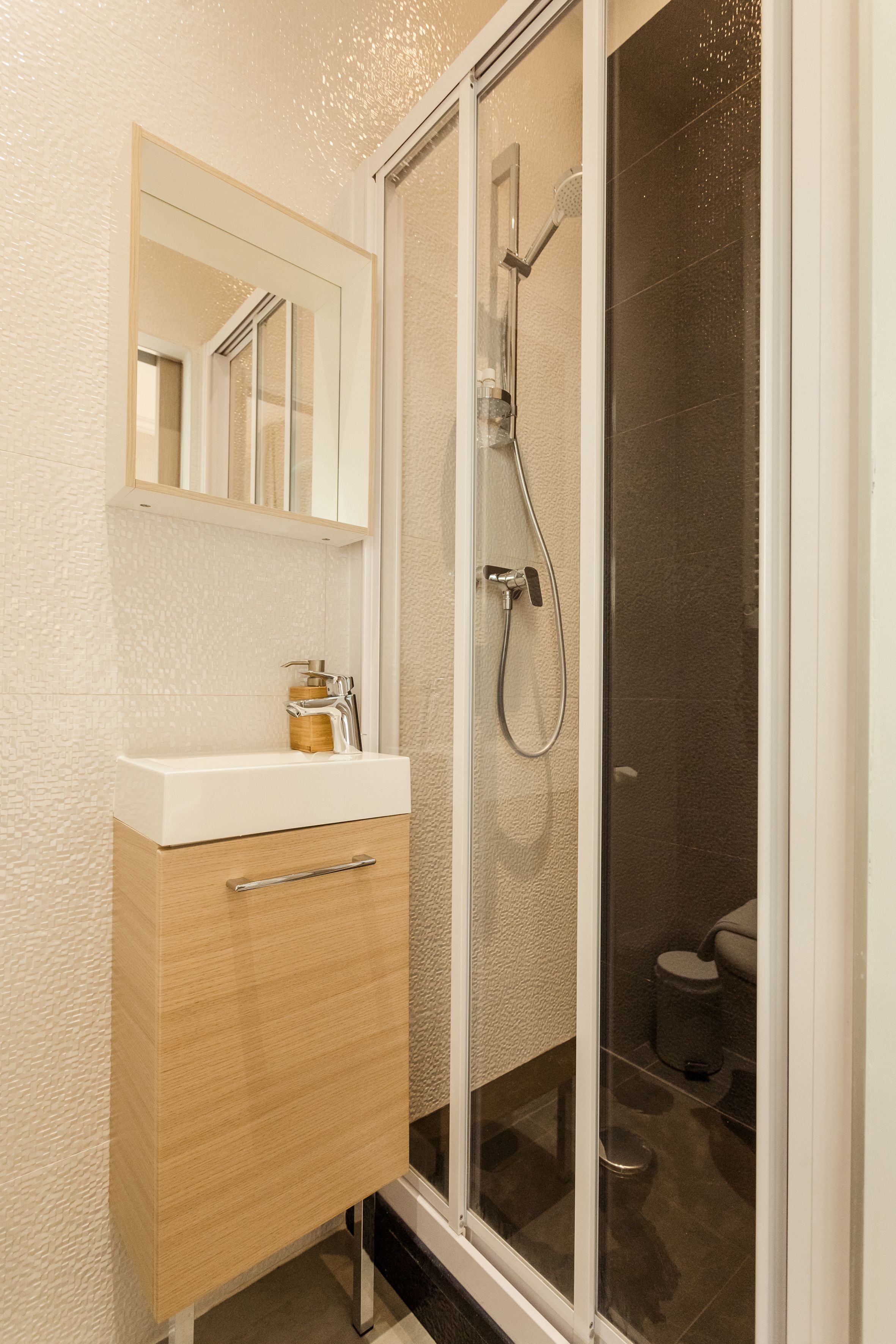 Une salle de bain moderne avec une douche à parois de verre, un meuble-lavabo en bois avec un miroir et un petit lavabo.
