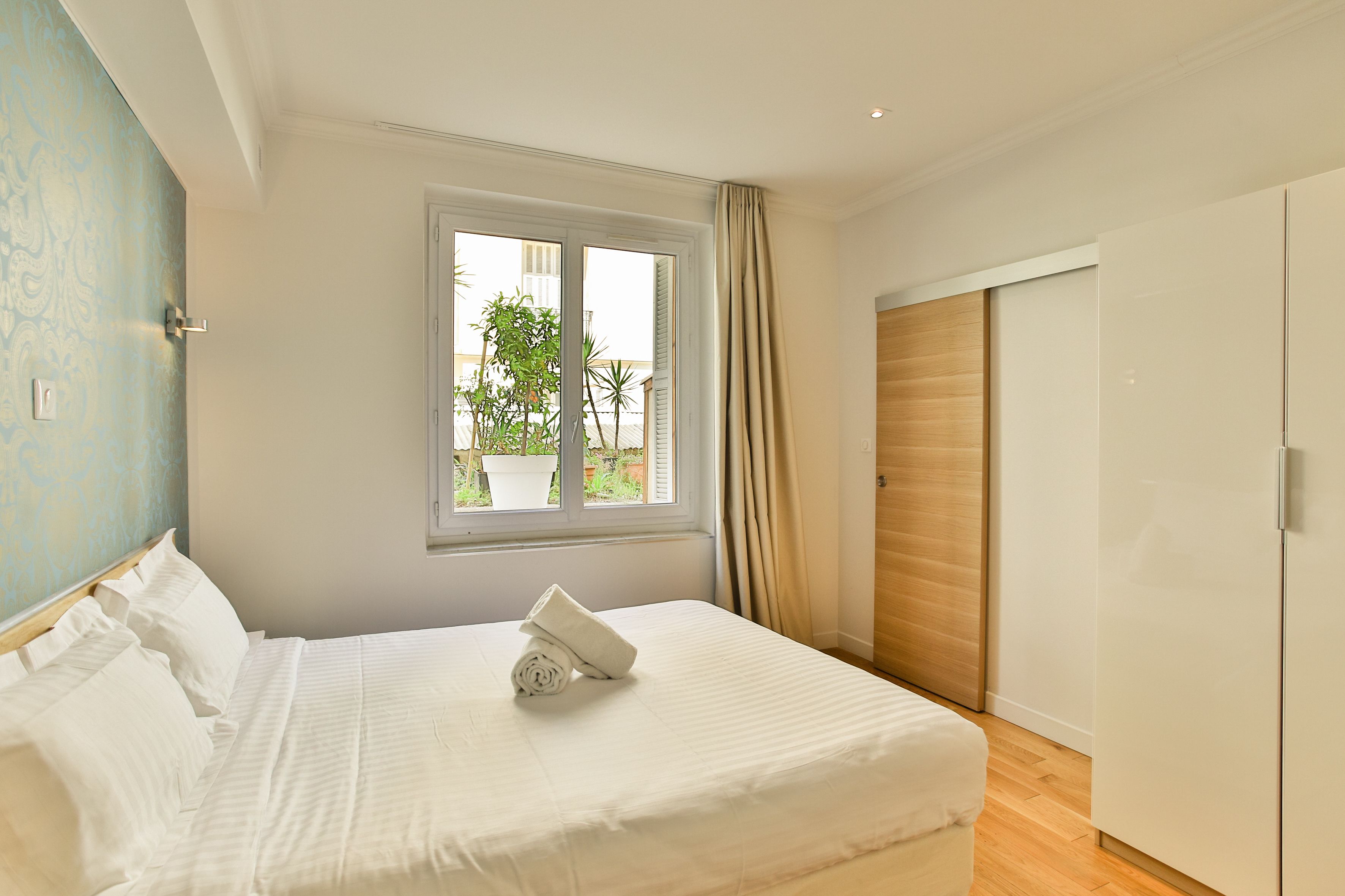 A bedroom with a bed, a window, a wardrobe, and a view of greenery outside.