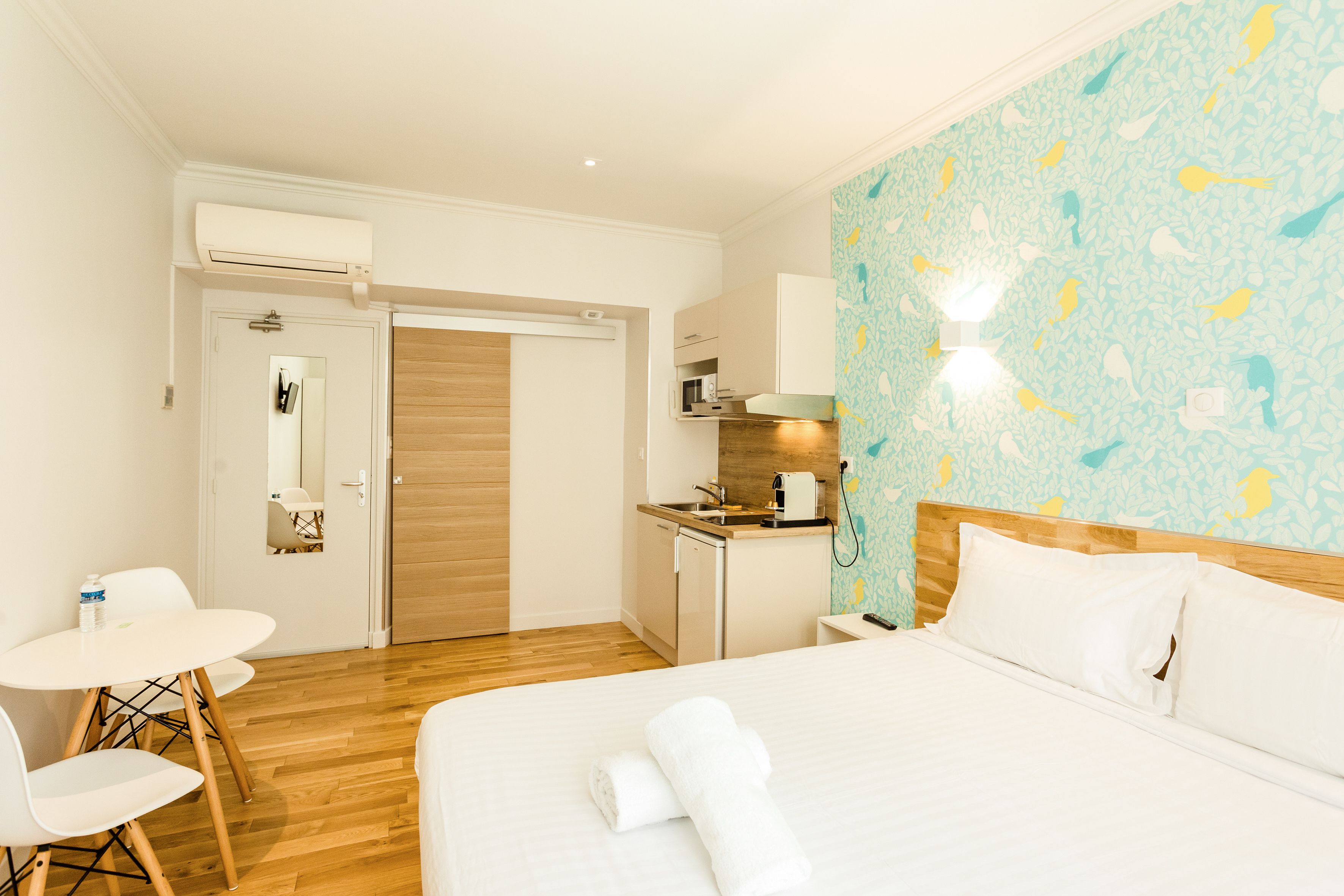 Una habitación de hotel con cama, escritorio, silla, kitchenette pequeño y baño.