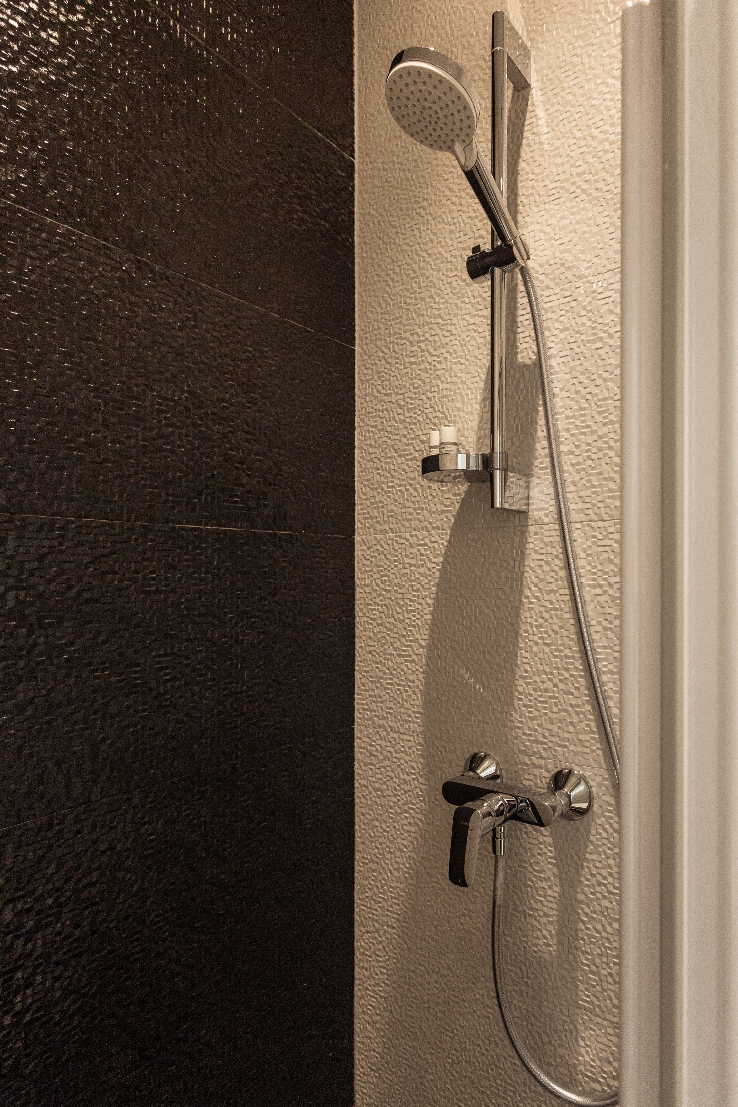 A bathroom with a shower, a handheld showerhead, and a wall-mounted faucet.