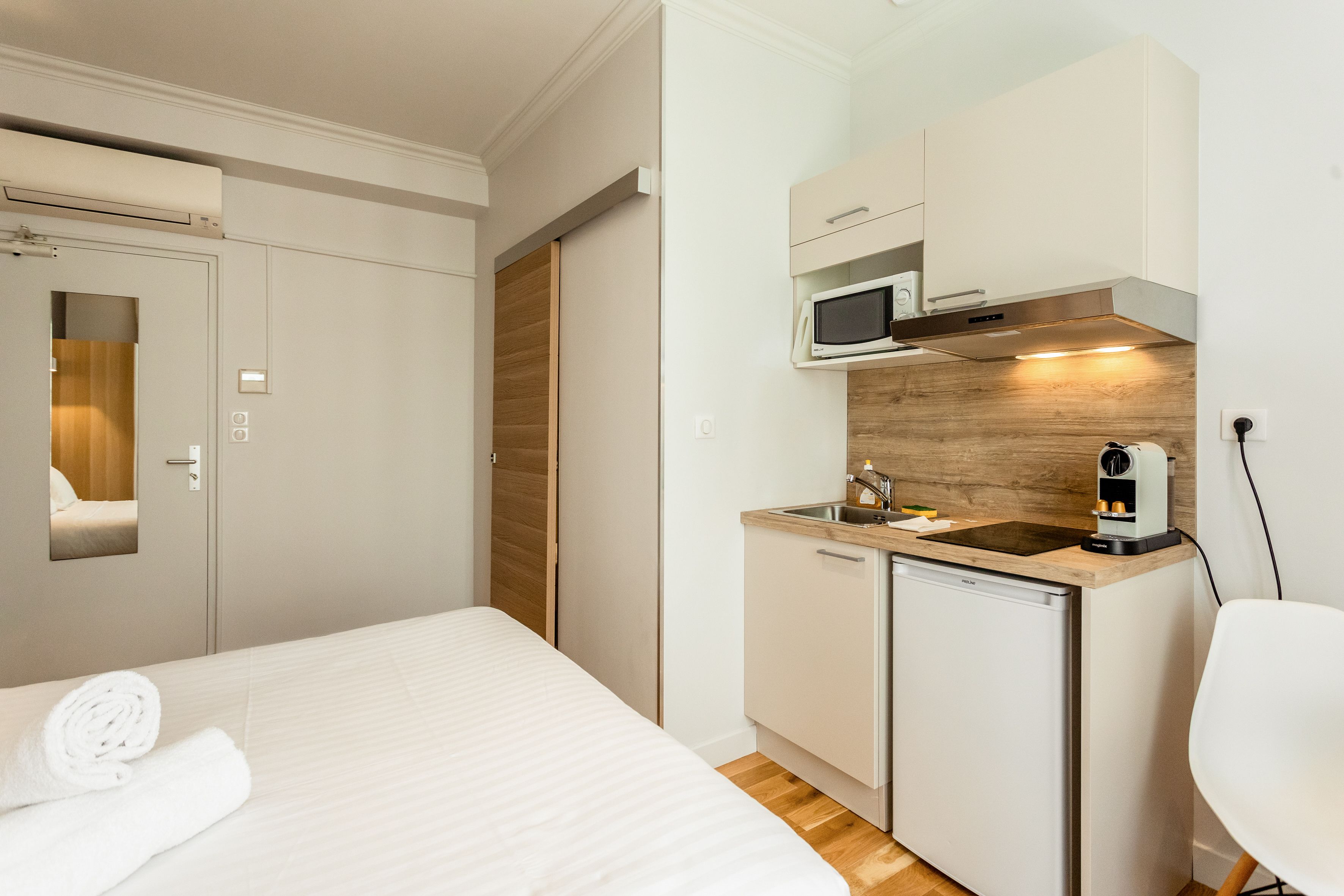 Ein kleines Hotelzimmer mit Bett, einer Küchenzeile und einem Spiegel.