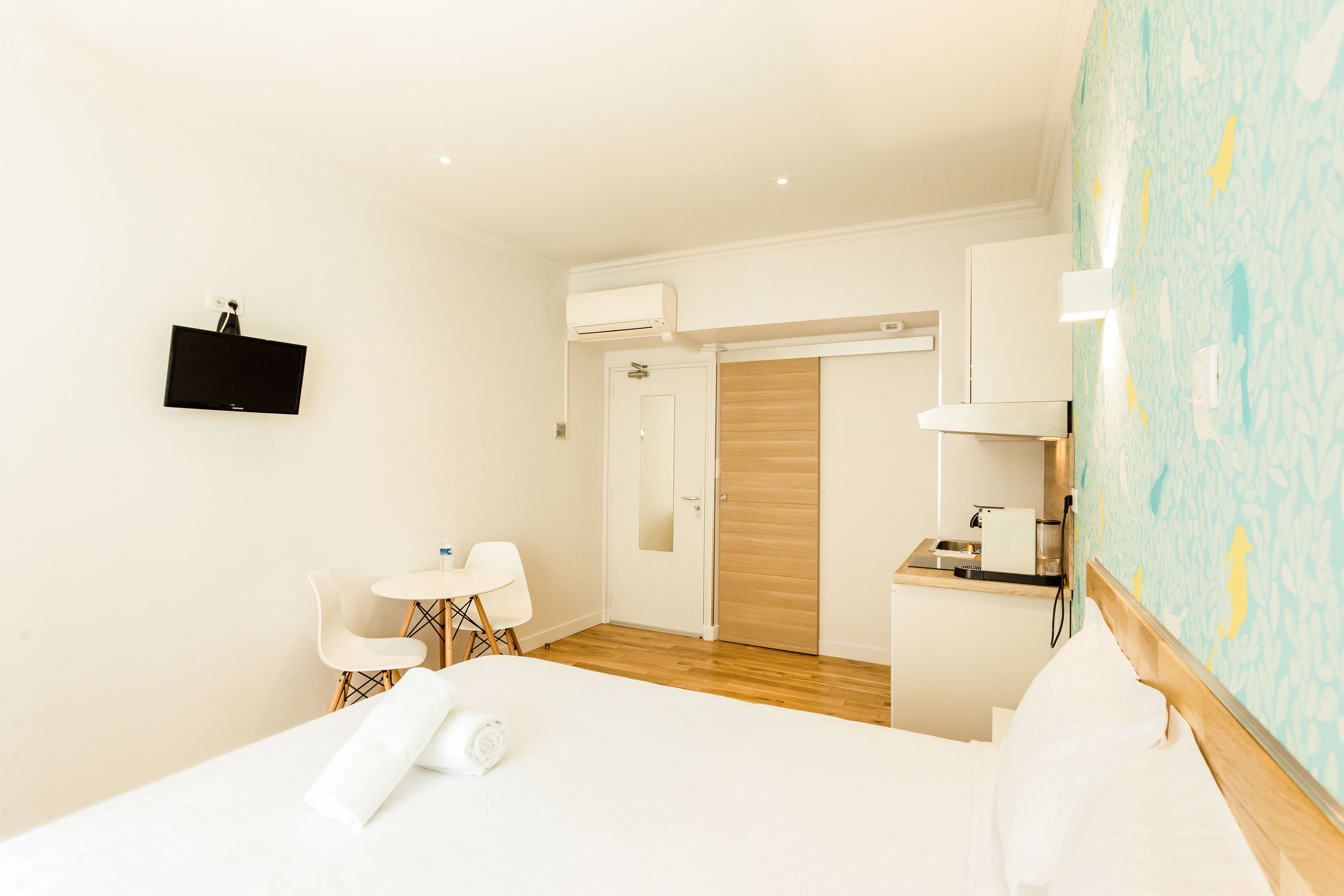 A hotel room with a bed, a desk, a chair, a small table, and a bathroom with a mirror and sink.
