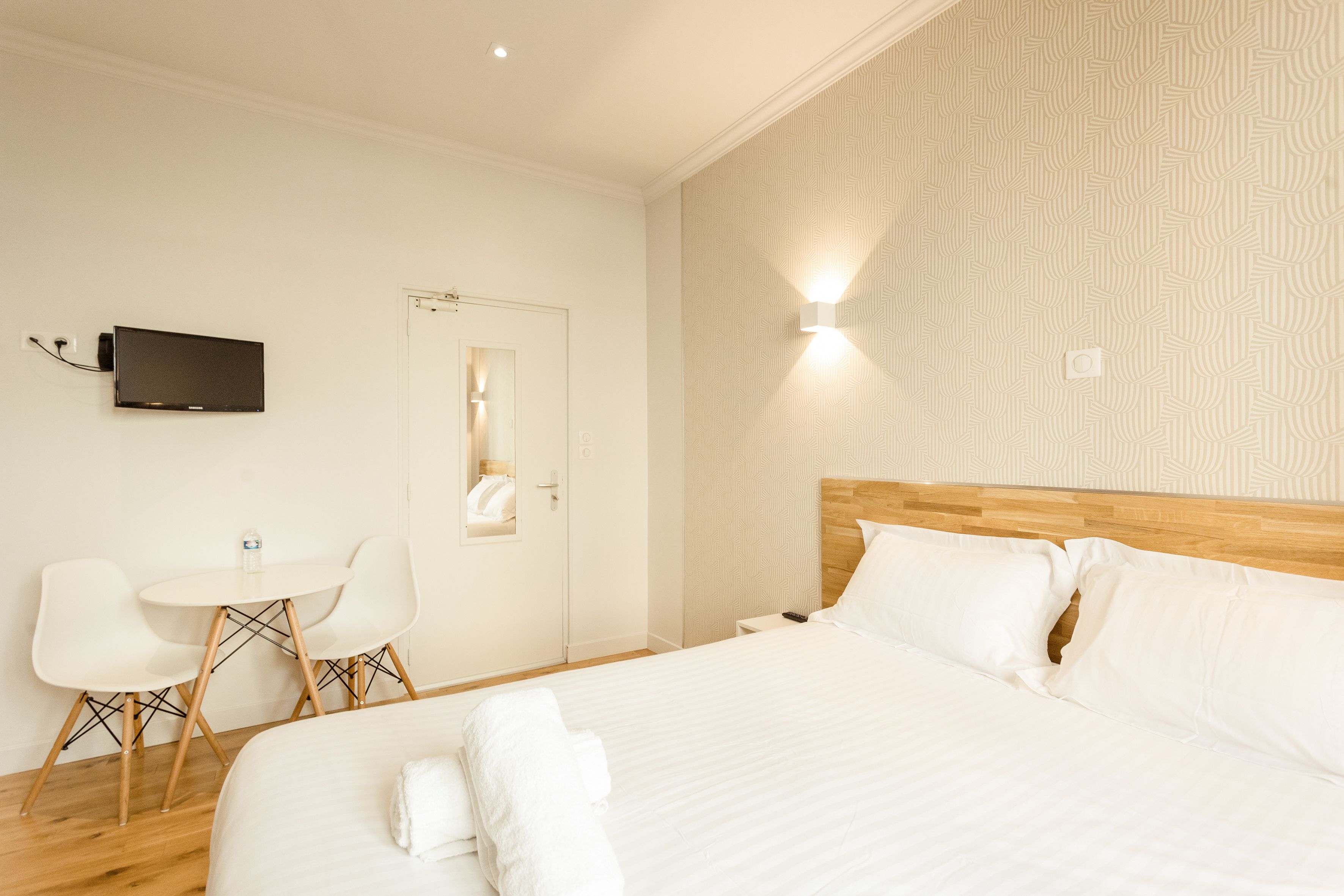 Habitació d'hotel amb un llit gran, una taula de nit, un televisor de pantalla plana fixat a la paret, una taula rodona petita amb dues cadires i un panell de fusta al capçal del llit.