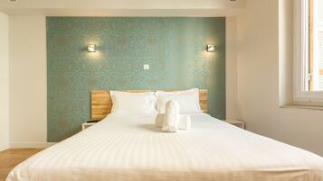 Een net opgemaakt bed met een witte deken en kussens, een houten hoofdbord en een muur met blauw behang met een patroon.