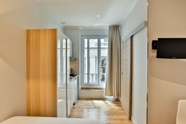 A hotel room with a wooden floor, a bed, a TV mounted on the wall, and a view of the balcony. - Nice Home - Studios Lido (Nice)