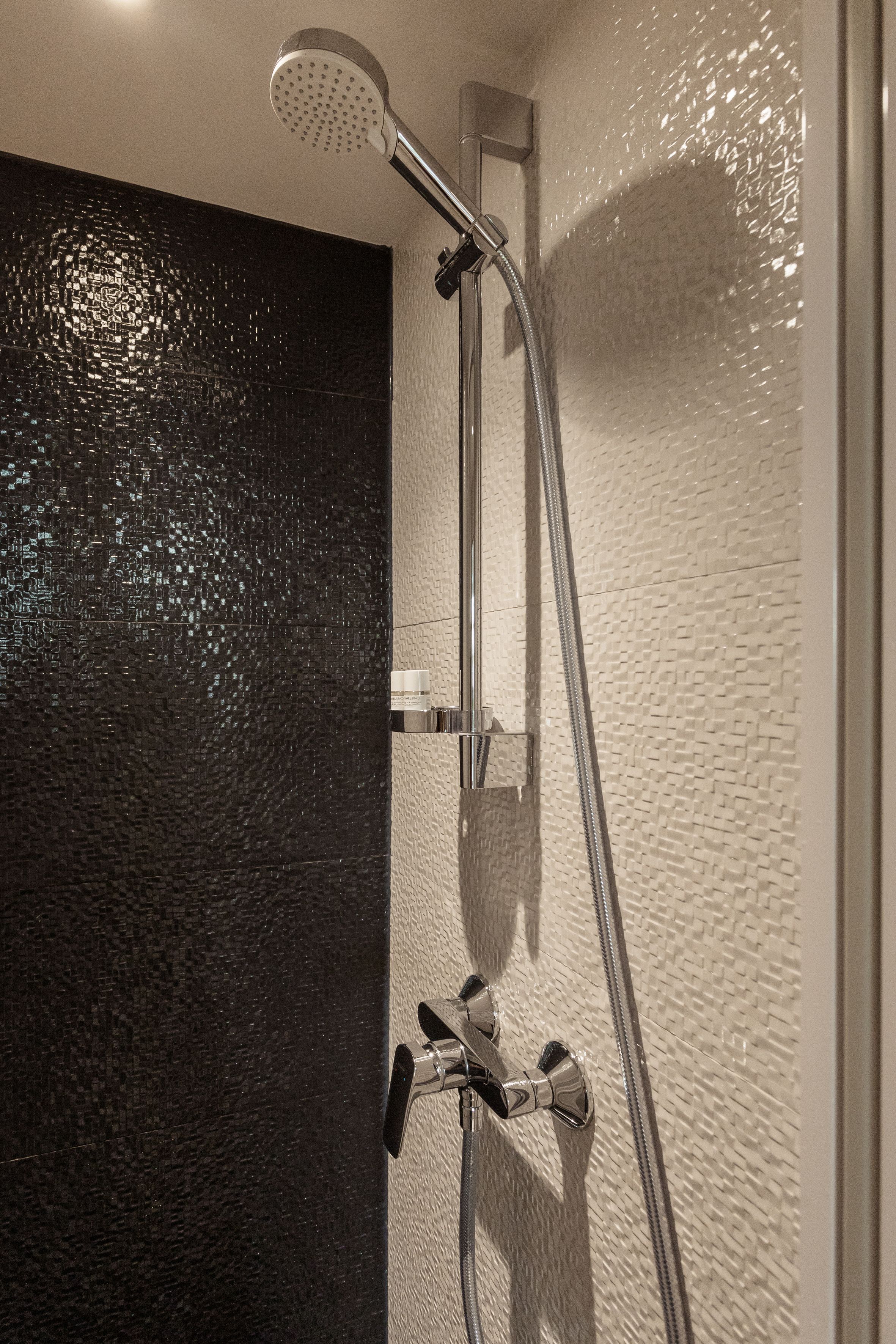 A shower with a handheld showerhead and a wall-mounted faucet.