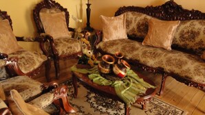 En traditionel stue med møbler i klassisk stil, heriblandt en sofa og lænestole med blomstret betræk, et træsofa bord med dekorative genstande, samt et tæppe med mønster.